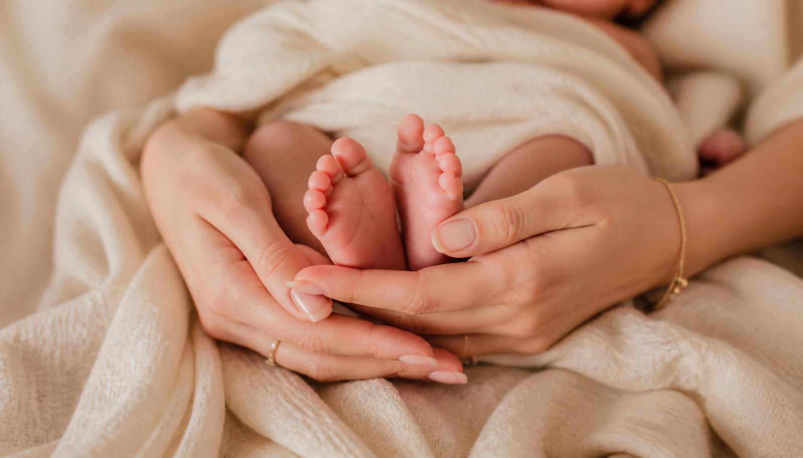 Mother's hands gently cradling a newborn wrapped in a soft blanket